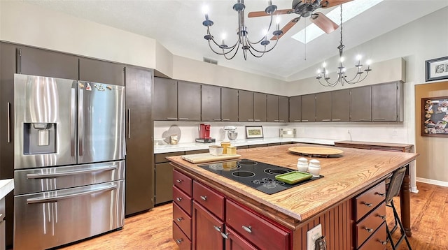 kitchen featuring stainless steel fridge, lofted ceiling with skylight, a kitchen island, decorative light fixtures, and black electric cooktop