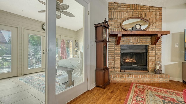 interior space with baseboards, a ceiling fan, wood finished floors, a textured ceiling, and a brick fireplace