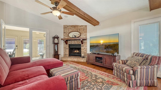 living room featuring a ceiling fan, wood finished floors, vaulted ceiling with beams, a textured ceiling, and a brick fireplace