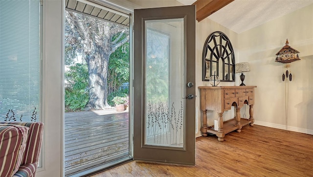 doorway featuring lofted ceiling with beams, light wood finished floors, and baseboards