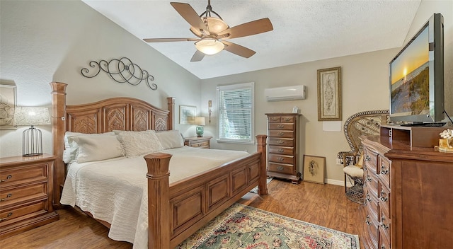 bedroom featuring ceiling fan, a textured ceiling, vaulted ceiling, an AC wall unit, and light wood-type flooring