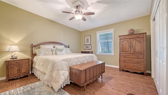 bedroom featuring a ceiling fan, a textured ceiling, baseboards, and wood finished floors