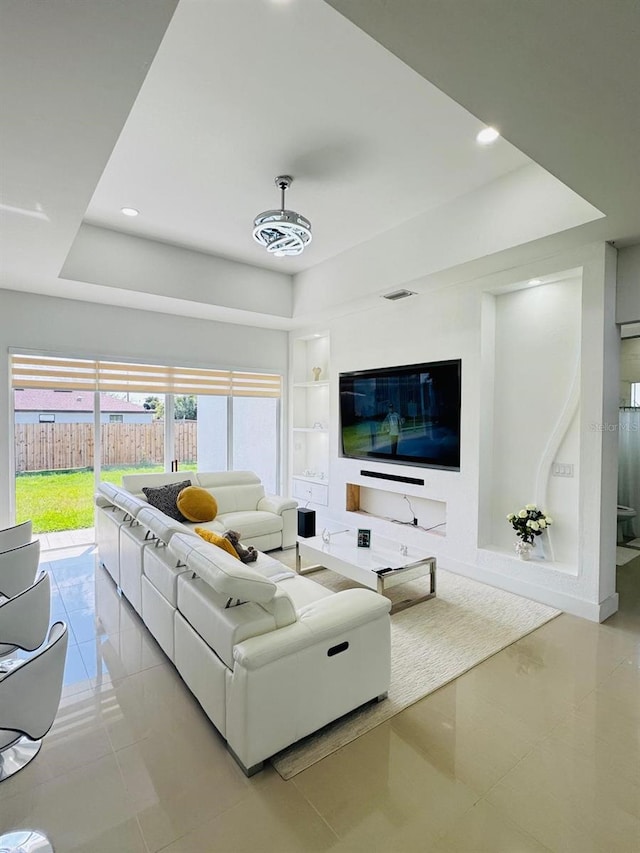 tiled living room with a raised ceiling, a healthy amount of sunlight, and built in shelves