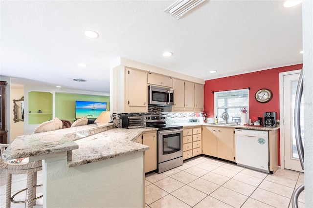 kitchen featuring appliances with stainless steel finishes, a peninsula, light stone countertops, cream cabinetry, and a kitchen bar