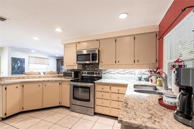 kitchen featuring cream cabinets, stainless steel appliances, a sink, light countertops, and tasteful backsplash
