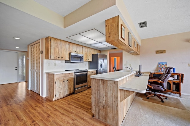 kitchen featuring stainless steel appliances, a peninsula, light countertops, and visible vents