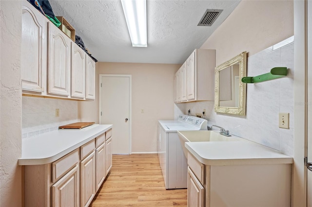 laundry room with washer and clothes dryer, visible vents, cabinet space, light wood-style flooring, and a textured ceiling