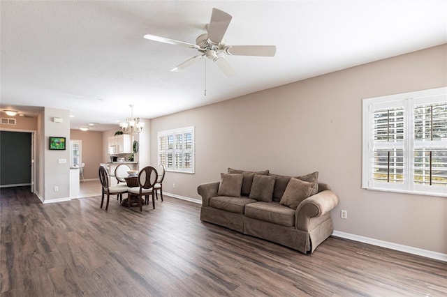 living area featuring ceiling fan with notable chandelier, dark wood finished floors, visible vents, and baseboards