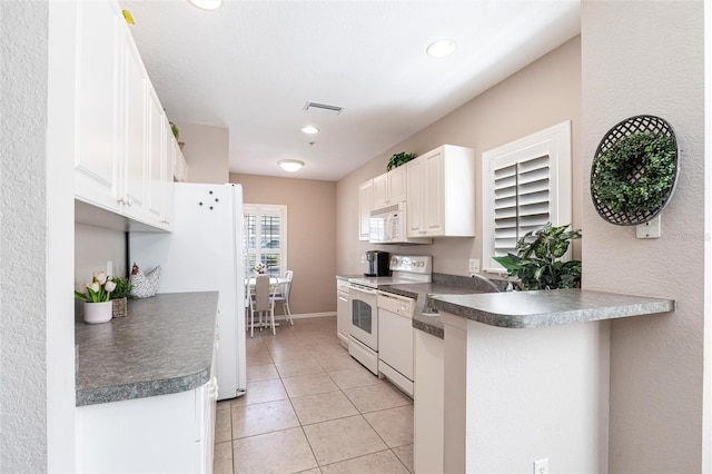 kitchen featuring dark countertops, visible vents, white cabinets, a sink, and white appliances