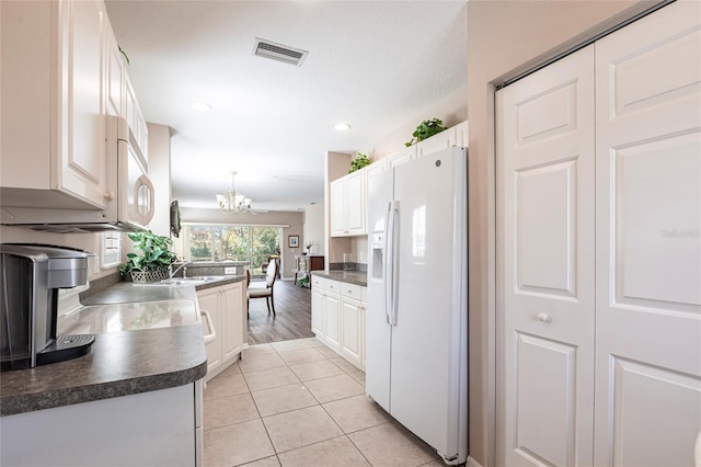 kitchen featuring dark countertops, white refrigerator with ice dispenser, and white cabinetry