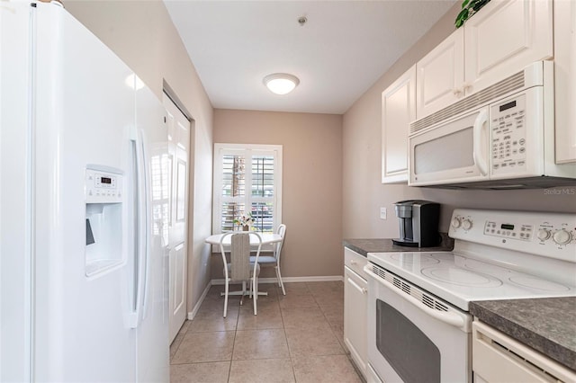 kitchen with white appliances, dark countertops, light tile patterned flooring, and white cabinets