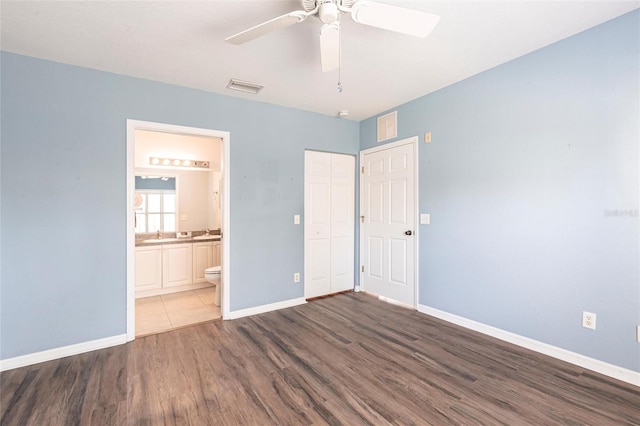 unfurnished bedroom with baseboards, visible vents, ensuite bath, wood finished floors, and a closet