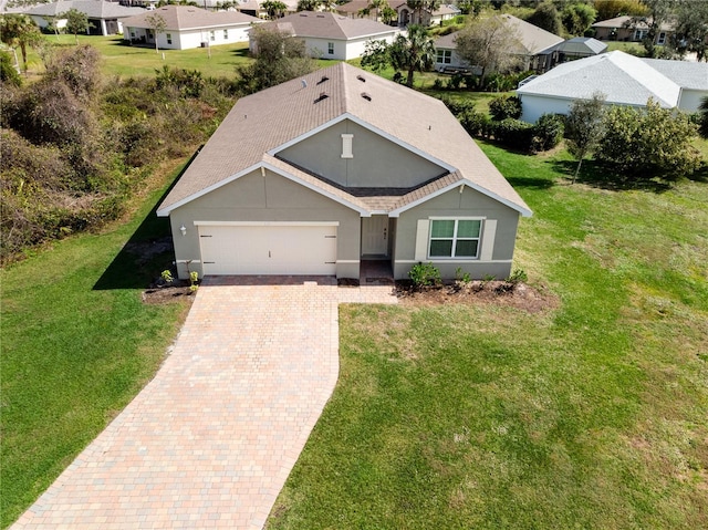 view of front of property with decorative driveway, stucco siding, a front yard, a garage, and a residential view