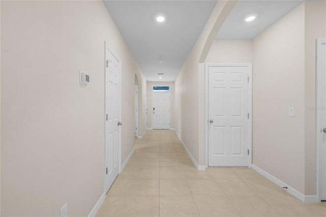 hall featuring arched walkways, recessed lighting, baseboards, and light tile patterned floors