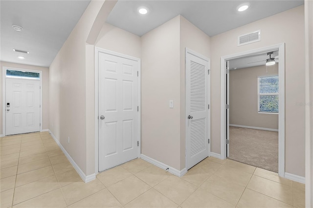 corridor featuring arched walkways, light tile patterned floors, visible vents, and baseboards