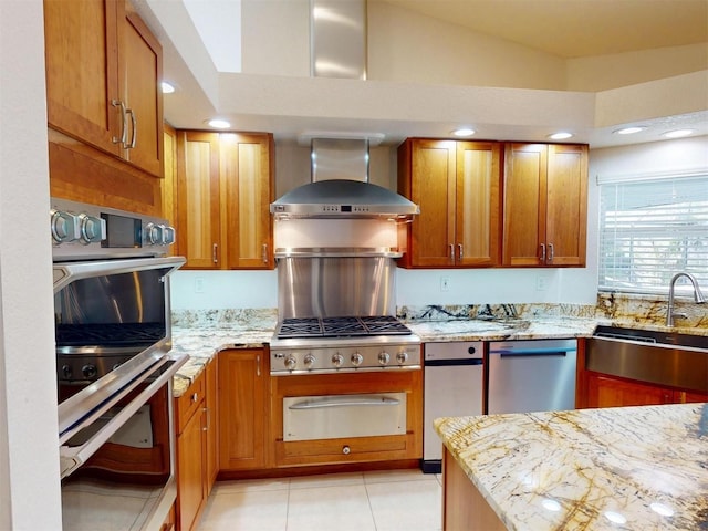 kitchen with light stone counters, a warming drawer, stainless steel appliances, a sink, and wall chimney exhaust hood