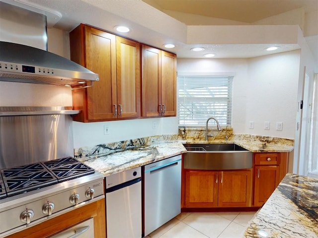 kitchen featuring stainless steel appliances, a sink, wall chimney range hood, and light stone countertops