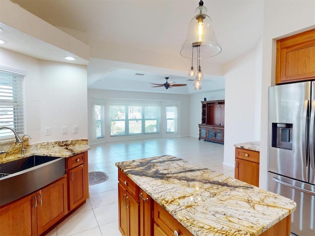 kitchen featuring plenty of natural light, light stone counters, stainless steel refrigerator with ice dispenser, and a sink