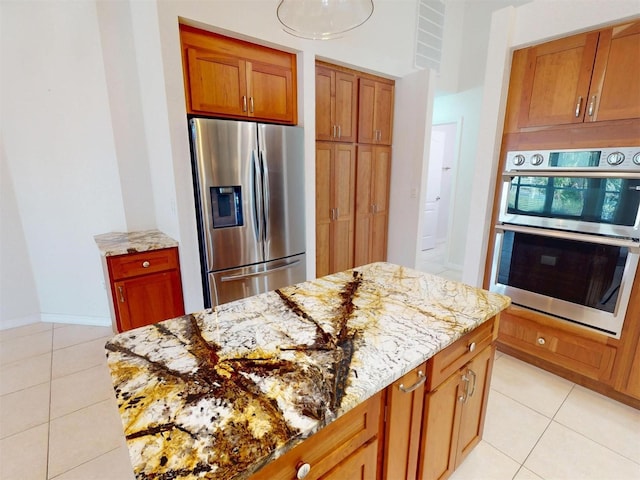 kitchen with light tile patterned floors, baseboards, appliances with stainless steel finishes, brown cabinets, and light stone countertops