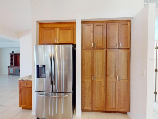 kitchen featuring light tile patterned floors, brown cabinets, stainless steel fridge with ice dispenser, and light stone countertops