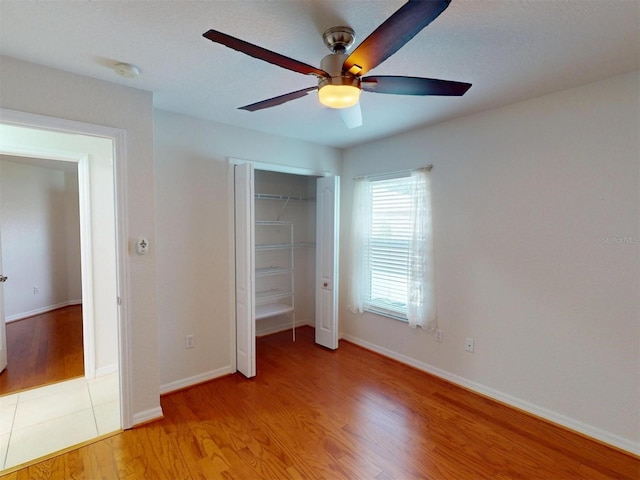 unfurnished bedroom with a closet, ceiling fan, light wood-style flooring, and baseboards