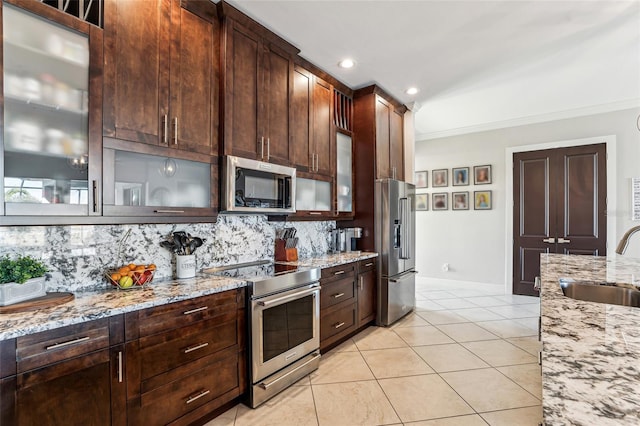 kitchen featuring light stone counters, appliances with stainless steel finishes, a sink, and glass insert cabinets