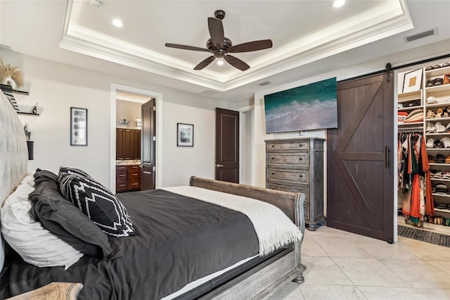 bedroom with a barn door, visible vents, a tray ceiling, a walk in closet, and crown molding