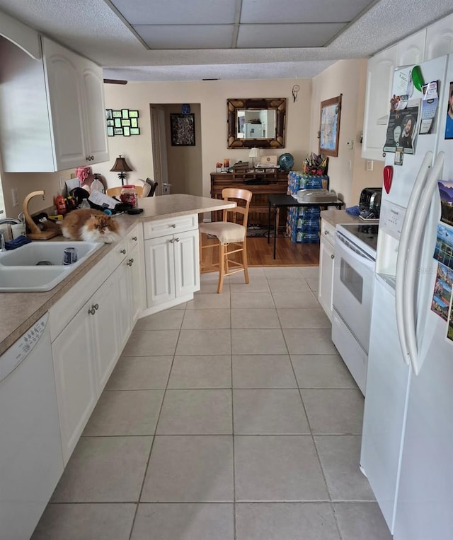 kitchen with light tile patterned flooring, white appliances, a sink, white cabinets, and light countertops