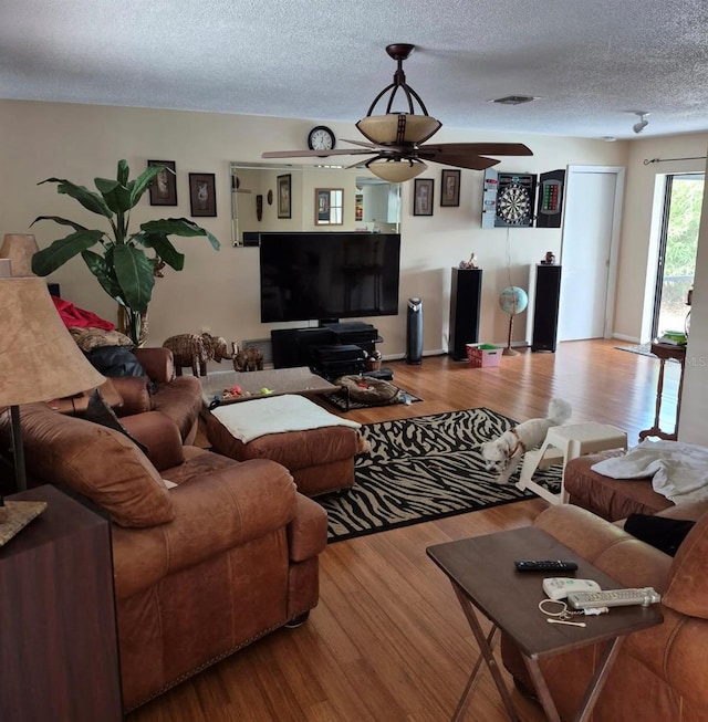 living area with a ceiling fan, visible vents, light wood-style flooring, and a textured ceiling