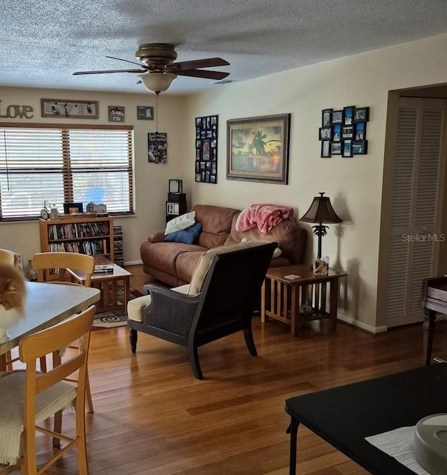 living room featuring a ceiling fan, a textured ceiling, baseboards, and wood finished floors