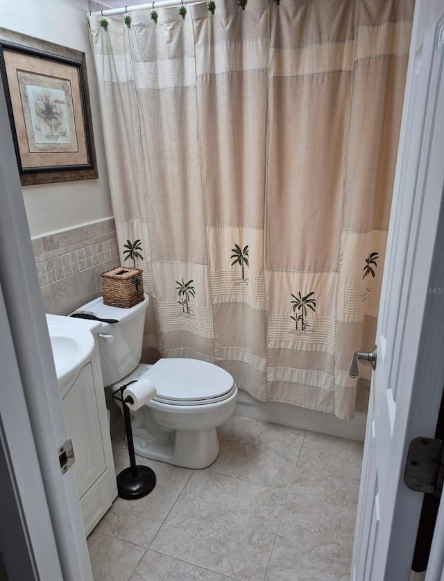 bathroom with wainscoting, toilet, tile patterned flooring, shower / bath combination with curtain, and tile walls