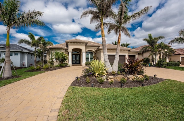 mediterranean / spanish home with a garage, a front lawn, decorative driveway, and stucco siding