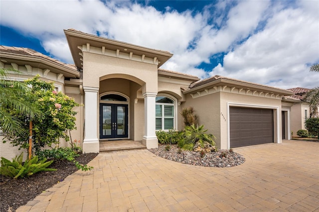 entrance to property featuring decorative driveway, french doors, a tile roof, stucco siding, and an attached garage