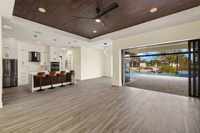 unfurnished living room with ceiling fan, light hardwood / wood-style flooring, a tray ceiling, and wooden ceiling