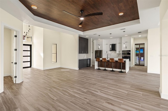 living room featuring a raised ceiling, light hardwood / wood-style flooring, ceiling fan, and wood ceiling