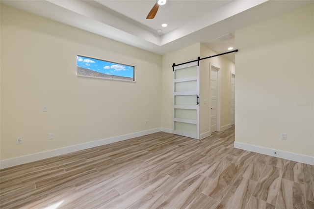 unfurnished bedroom with ceiling fan, a barn door, and light wood-type flooring