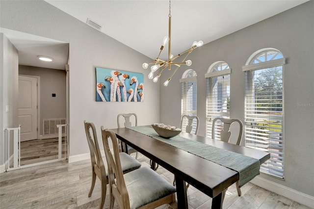 dining area with light wood-type flooring, an inviting chandelier, and vaulted ceiling