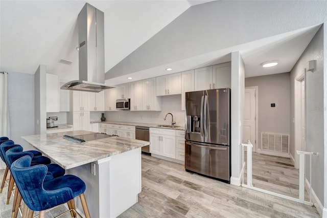 kitchen featuring kitchen peninsula, a breakfast bar, appliances with stainless steel finishes, white cabinets, and island exhaust hood