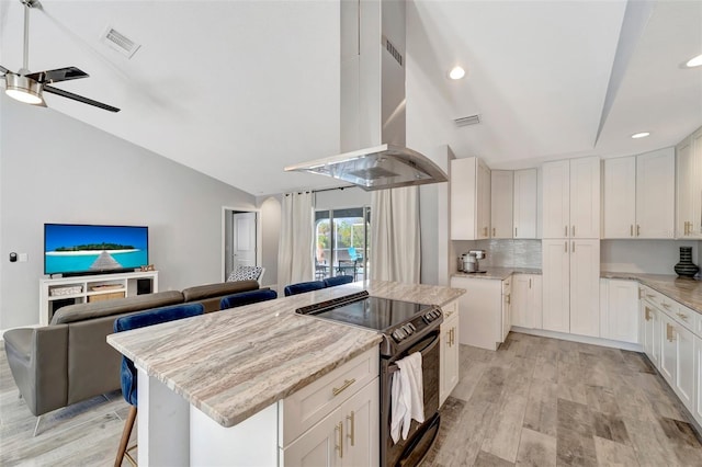 kitchen with light stone counters, island range hood, white cabinetry, a kitchen island, and black / electric stove