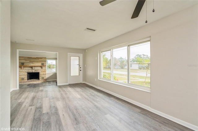 unfurnished living room featuring ceiling fan, a stone fireplace, visible vents, baseboards, and light wood-type flooring