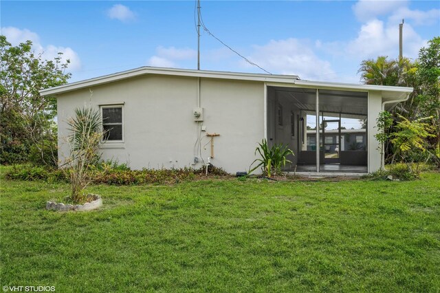 rear view of house featuring a sunroom, a lawn, and stucco siding