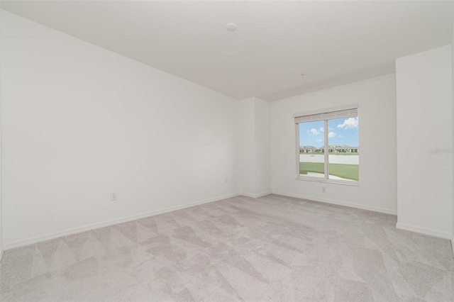 spare room featuring light carpet and baseboards