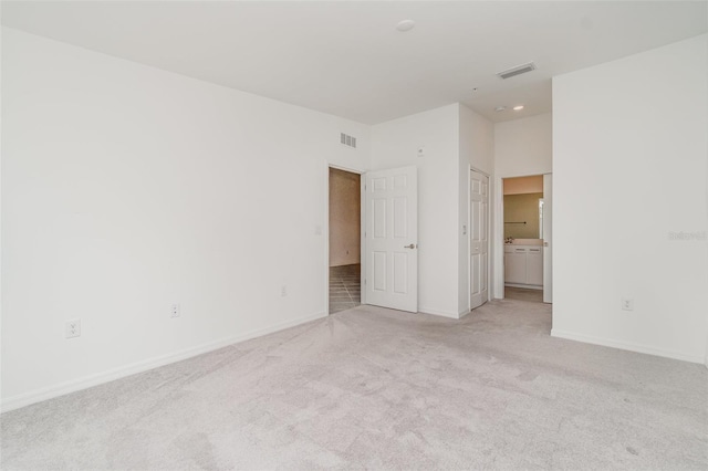 unfurnished bedroom featuring baseboards, visible vents, ensuite bathroom, and light colored carpet