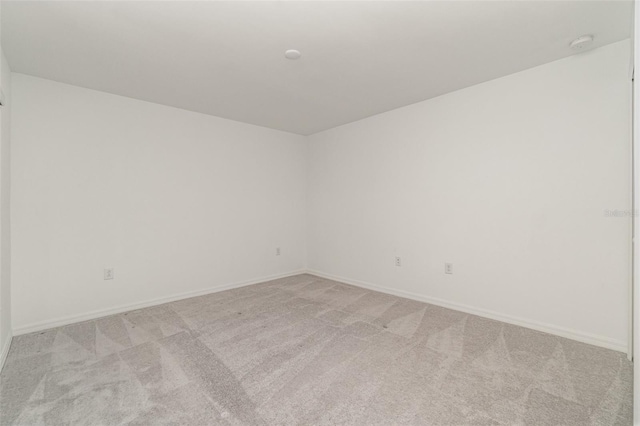 spare room with baseboards and light colored carpet