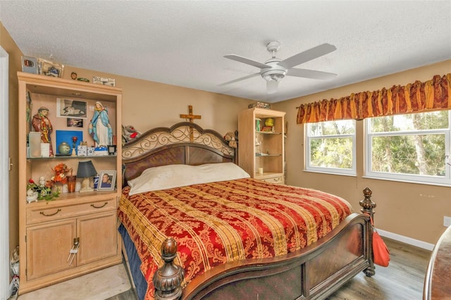 bedroom with a textured ceiling, light wood-type flooring, a ceiling fan, and baseboards