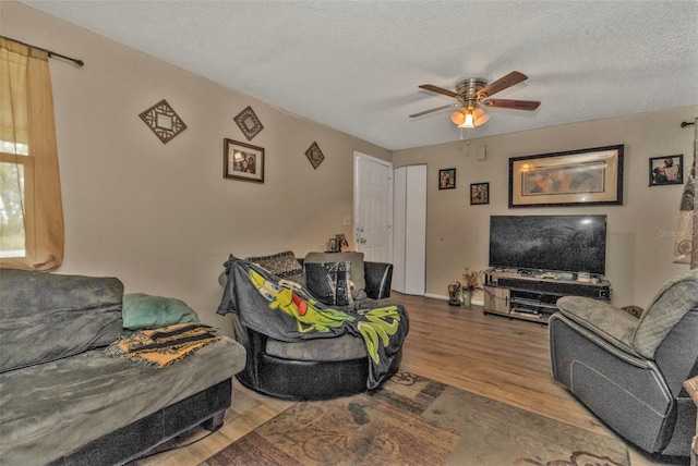 living area with ceiling fan, a textured ceiling, and wood finished floors