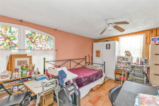 bedroom with wood walls, ceiling fan, a textured ceiling, and freestanding refrigerator