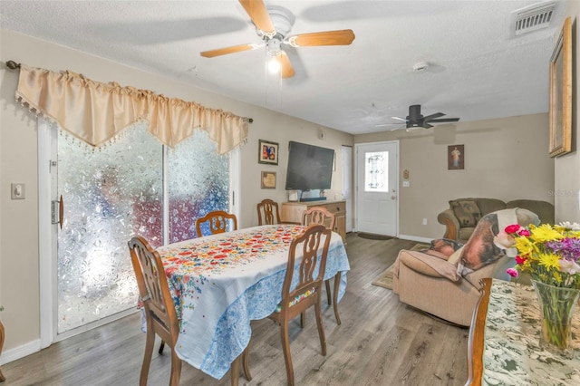 dining room with a textured ceiling, light wood-style flooring, a ceiling fan, visible vents, and baseboards