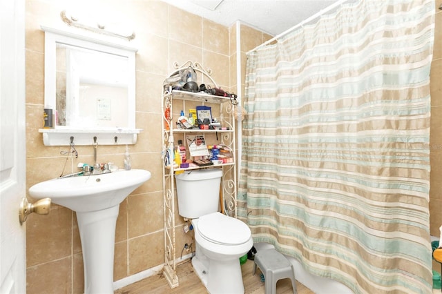 bathroom featuring tile walls, toilet, a shower with shower curtain, a sink, and wood finished floors