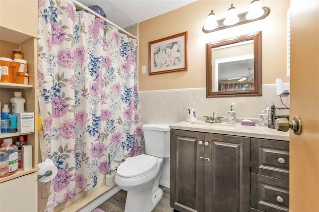 bathroom with toilet, a wainscoted wall, a textured ceiling, vanity, and tile walls